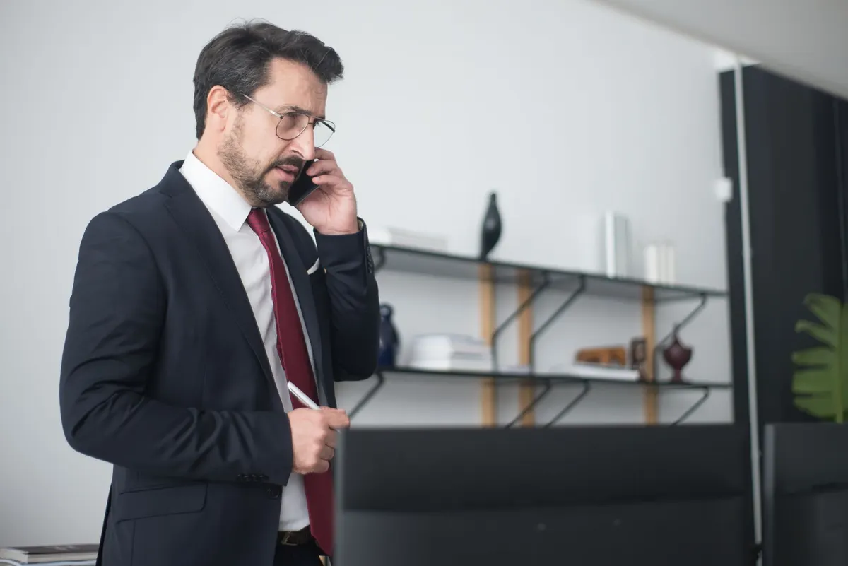 Businessman in suit speaking on mobile phone in modern office setting.