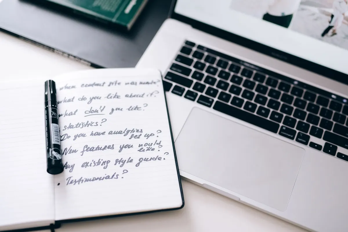 A notebook with handwritten notes next to a laptop on a workspace desk.